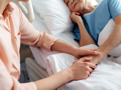cropped view of daughter sitting near senior mother in bed and holding hands in hospital