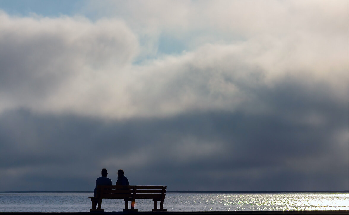 Women sit on bench overlooking ocean